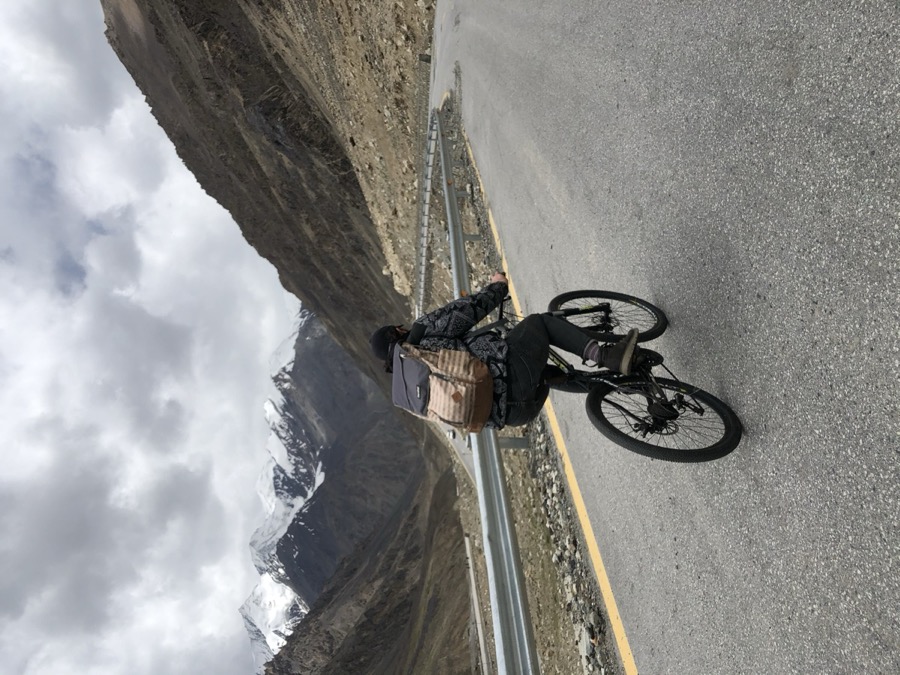 Talha cycling on a mountain road with snow-capped peaks behind